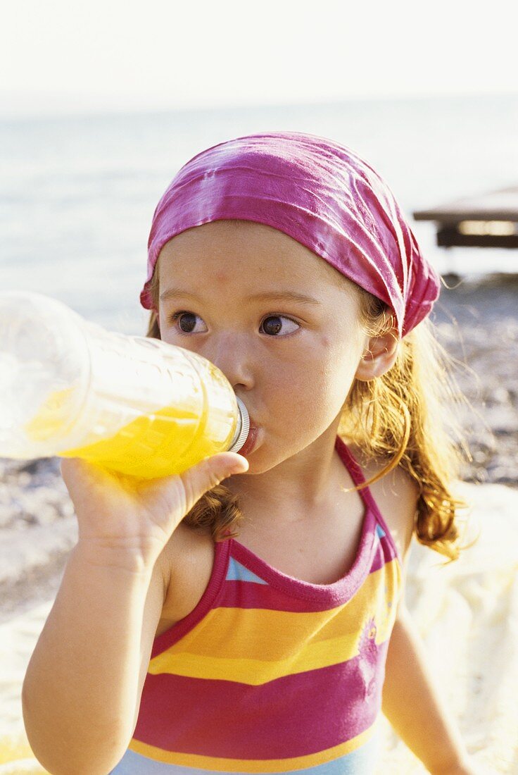 Mädchen am Strand trinkt aus einer Plastikflasche
