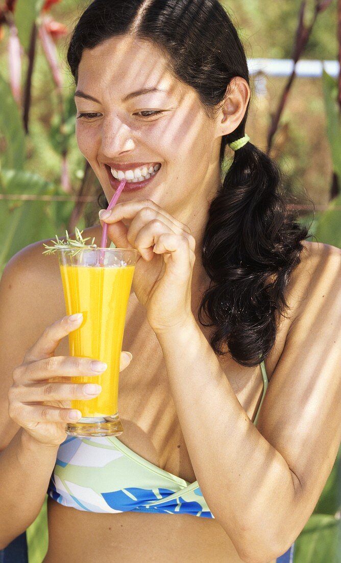 Young woman in bikini drinking orange juice