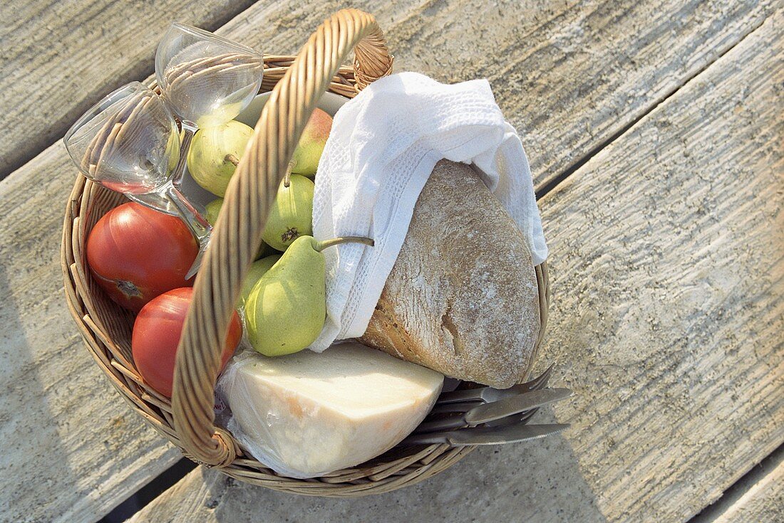 Korb mit Tomaten, Birnen, Käse, Brot und Gläsern
