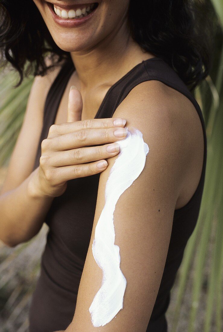Young woman putting lotion on her arm