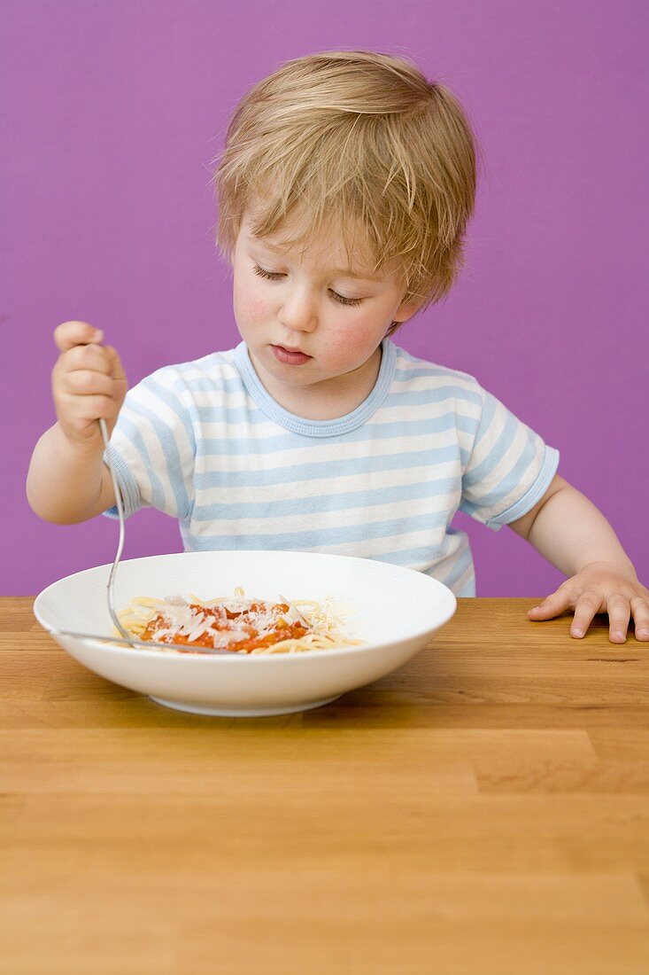 Small boy eating spaghetti with tomato sauce