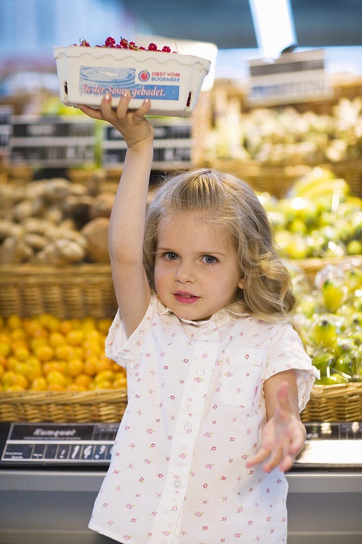Kleines Mädchen hebt Schale mit Johannisbeeren im Supermarkt
