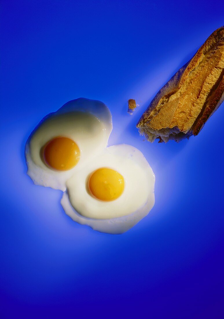 Two fried eggs and baguette on blue background