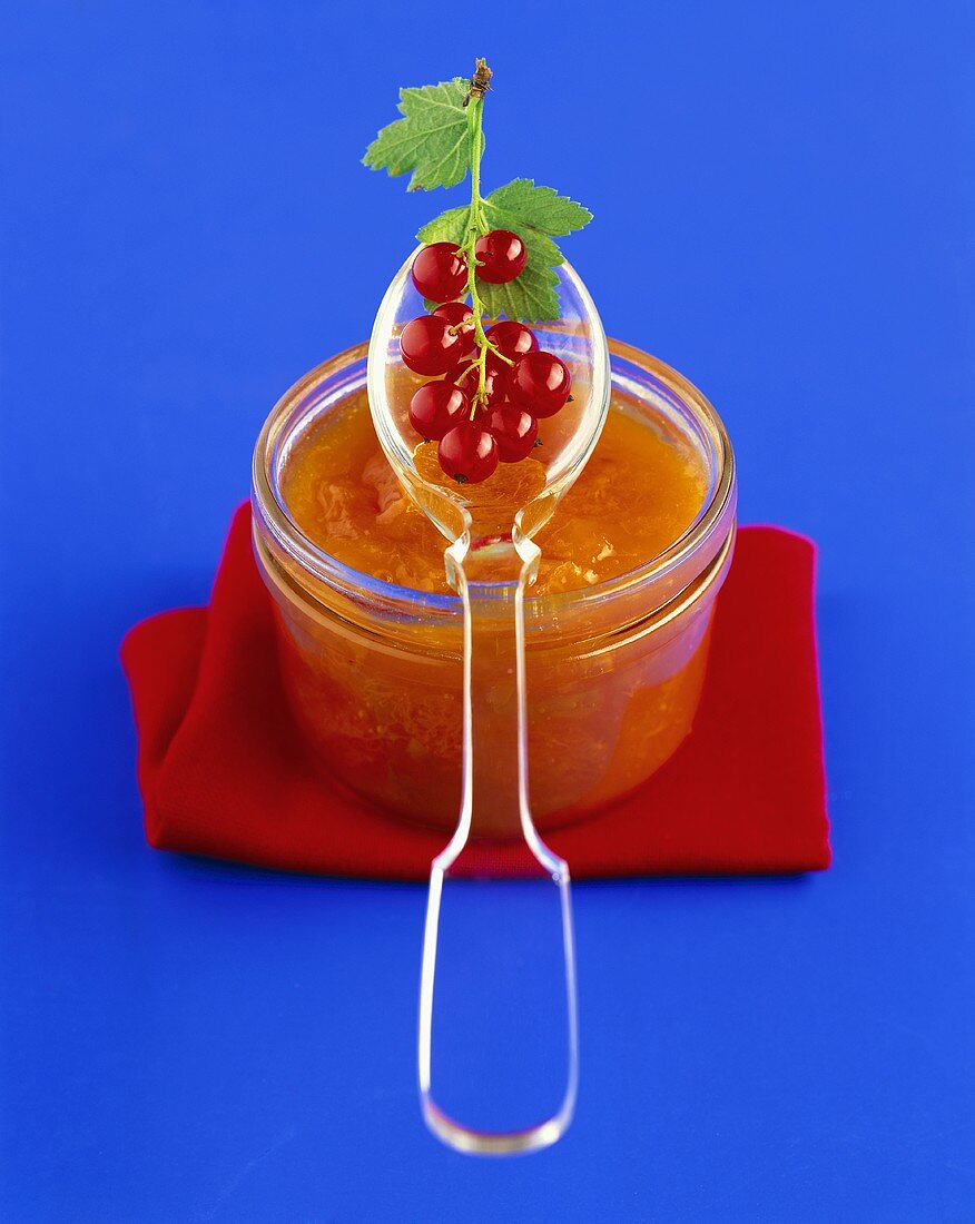 Aprikosenmarmelade im Glas, darauf Löffel mit Johannisbeeren