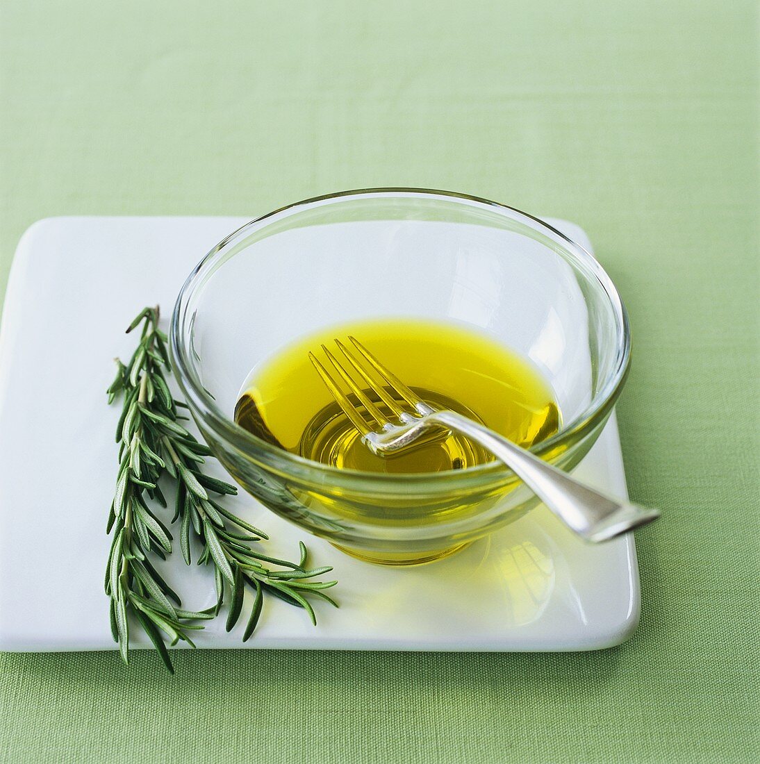 Olive oil in small glass bowl with fork, rosemary beside it