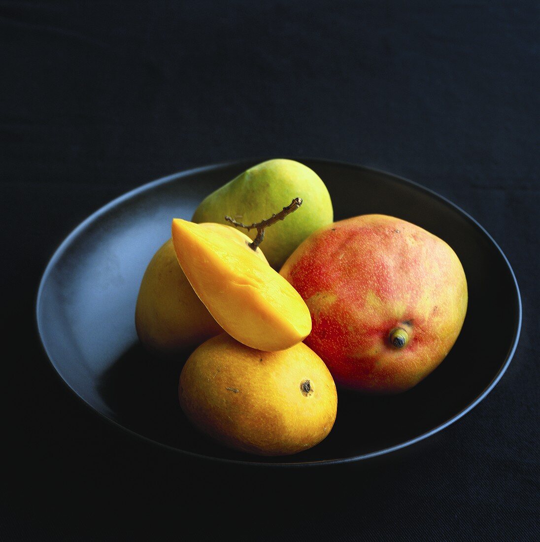 Verschiedene Mangos auf schwarzem Teller