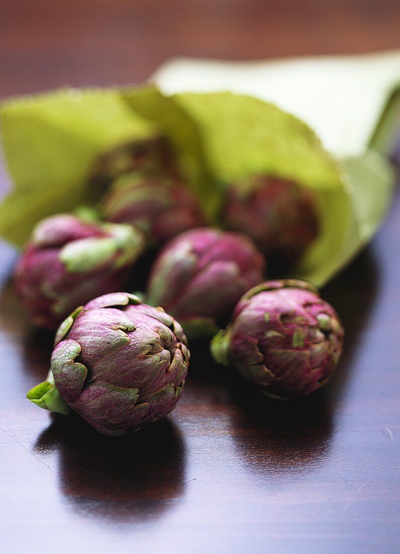 Purple artichokes in front of green paper bag