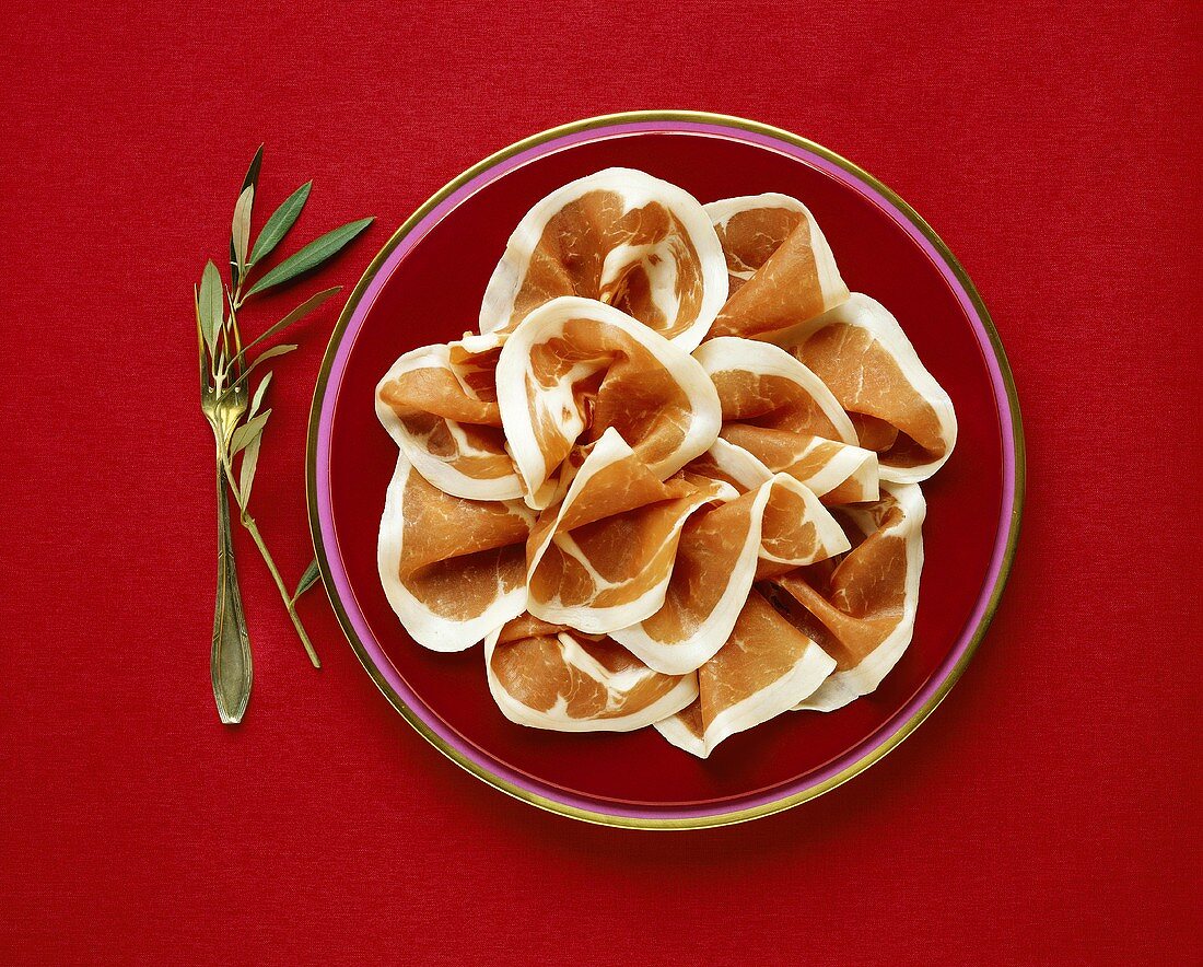 Parmaschinkenscheiben auf rotem Teller; Olivenzweig