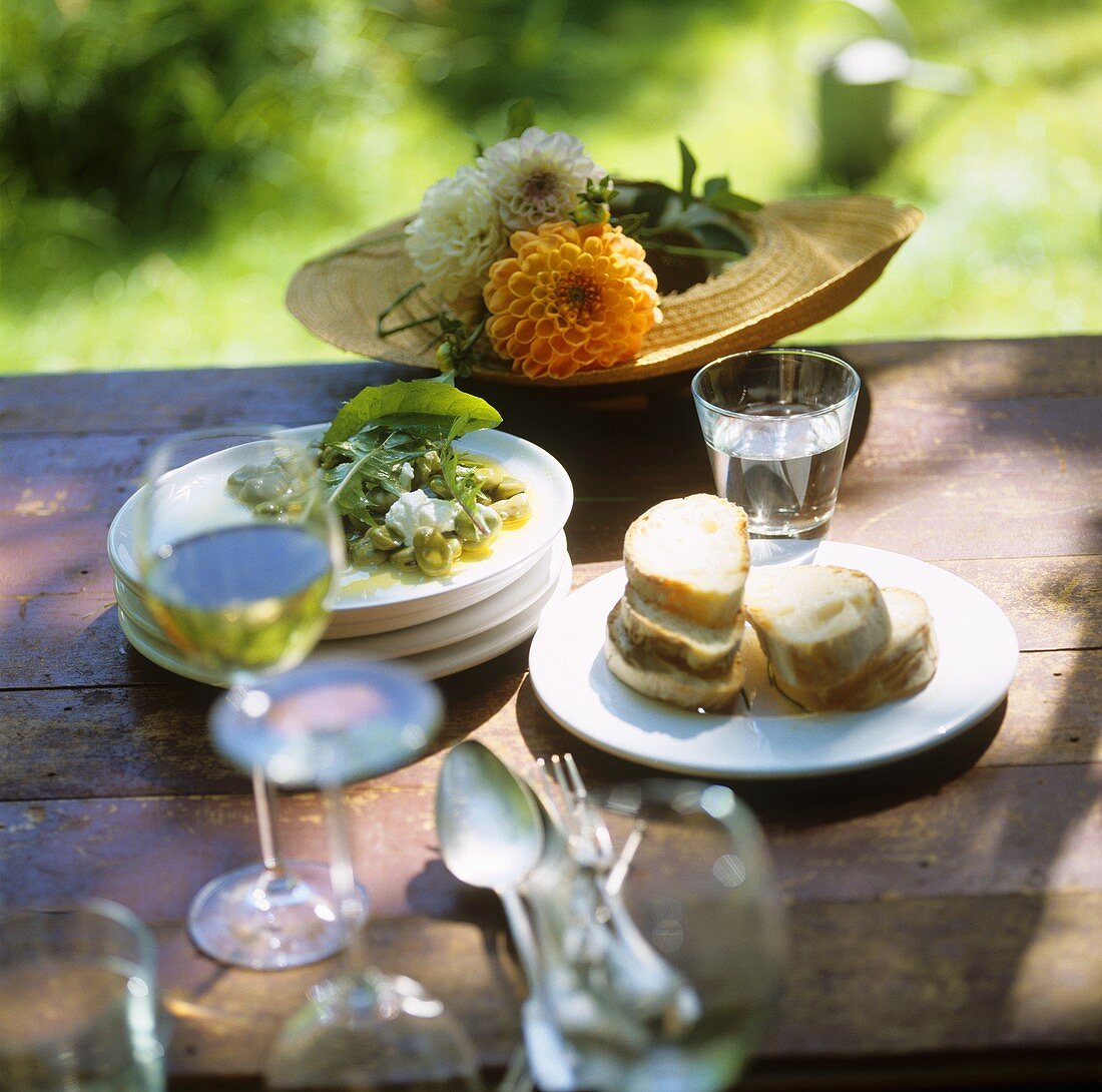 Bohnensalat mit Frischkäse und Weißbrot auf Tisch im Garten