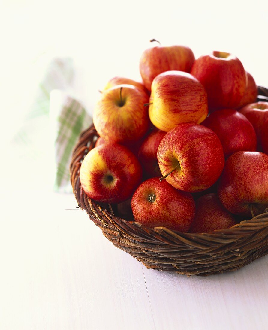 Rote Äpfel im Weidenkorb auf weißem Untergrund