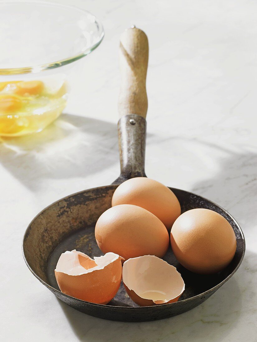 Vier braune Eier, eines aufgeschlagen, in Pfanne