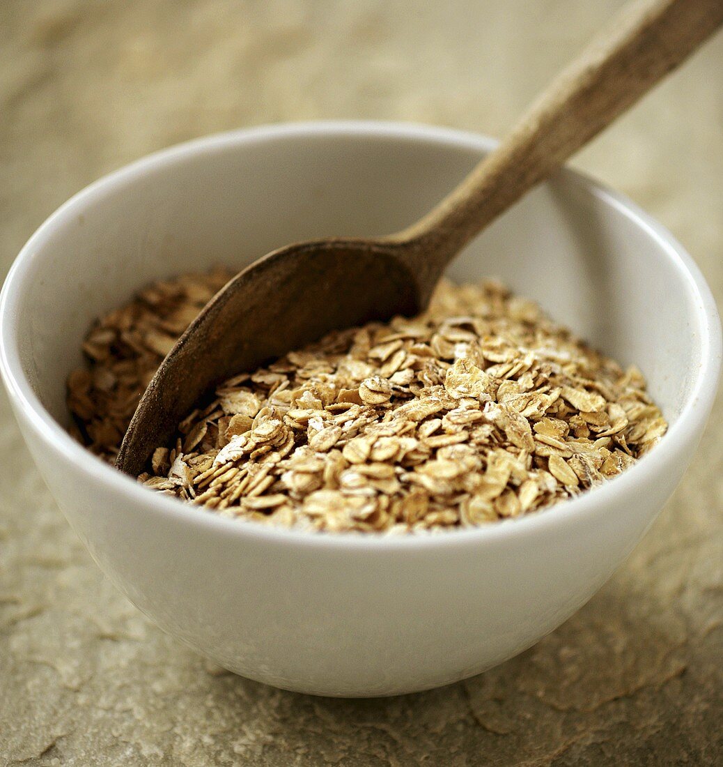 Rolled oats in white bowl with wooden spoon