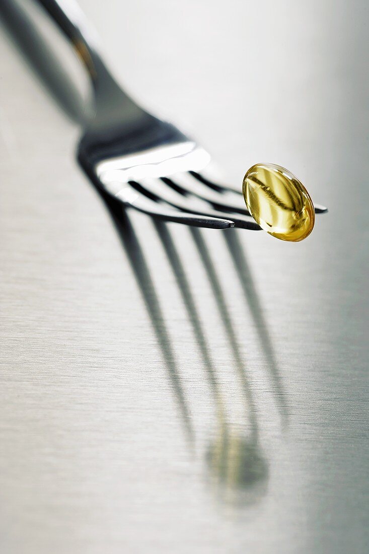 Yellow vitamin capsule on fork