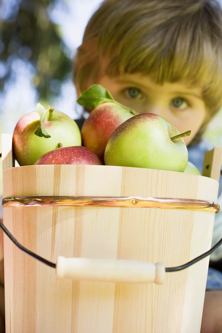 Kind hinter Holzeimer mit Äpfeln
