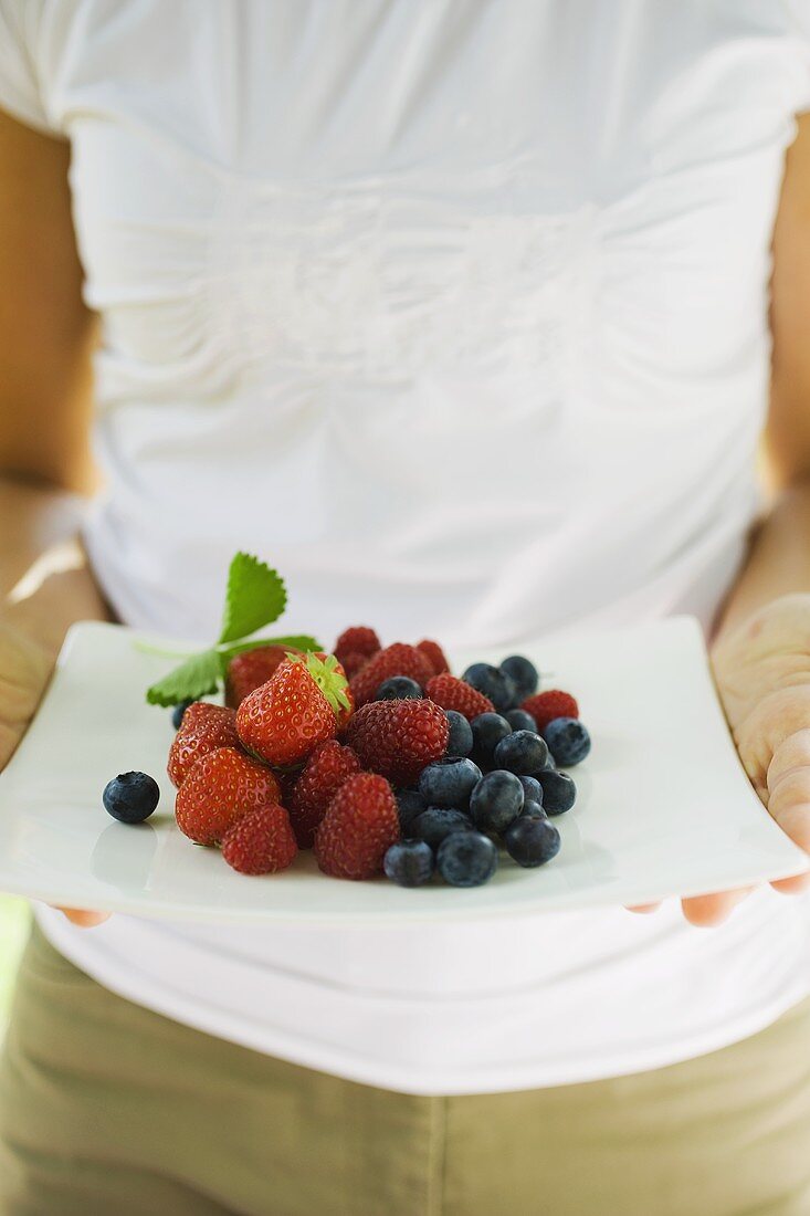 Frau hält Platte mit frischen Beeren