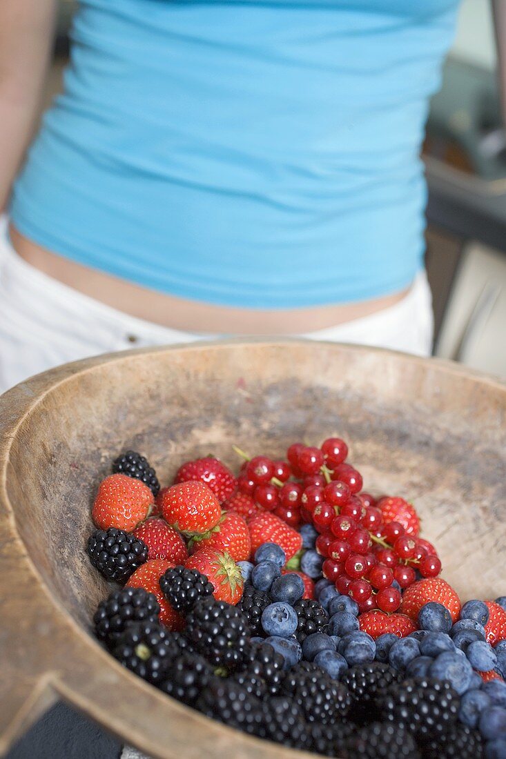 Fresh berries in bowl, woman in background