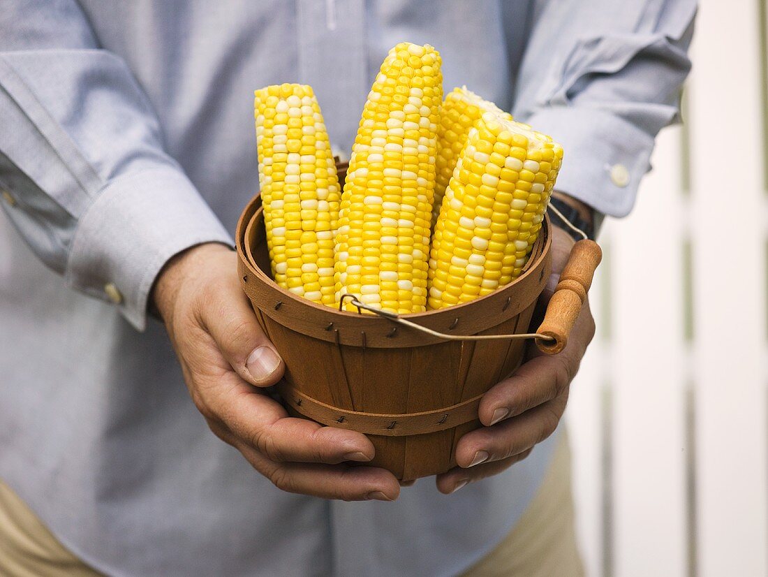 Man holding woodchip basket full of corn cobs