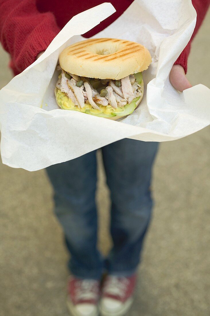 Person hält Bagel mit Schweinefilet, Kapern und Senfrelish