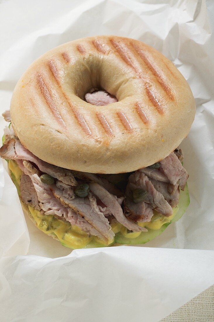 Pork fillet, capers and mustard relish in bagel on paper