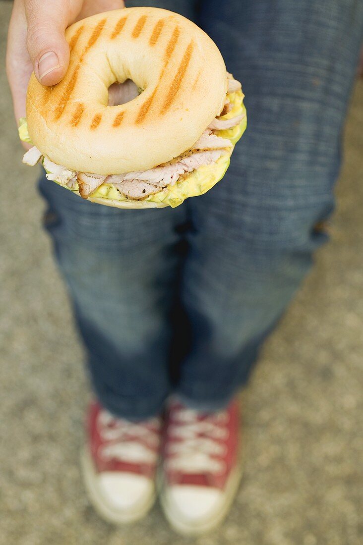 Person hält Bagel mit Schweinefilet, Kapern und Senfrelish