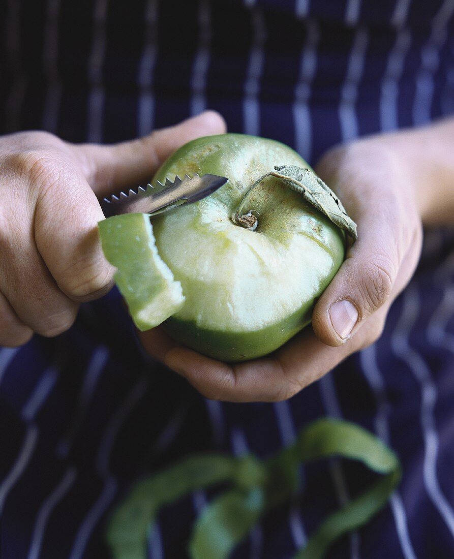 Hands peeling a green apple