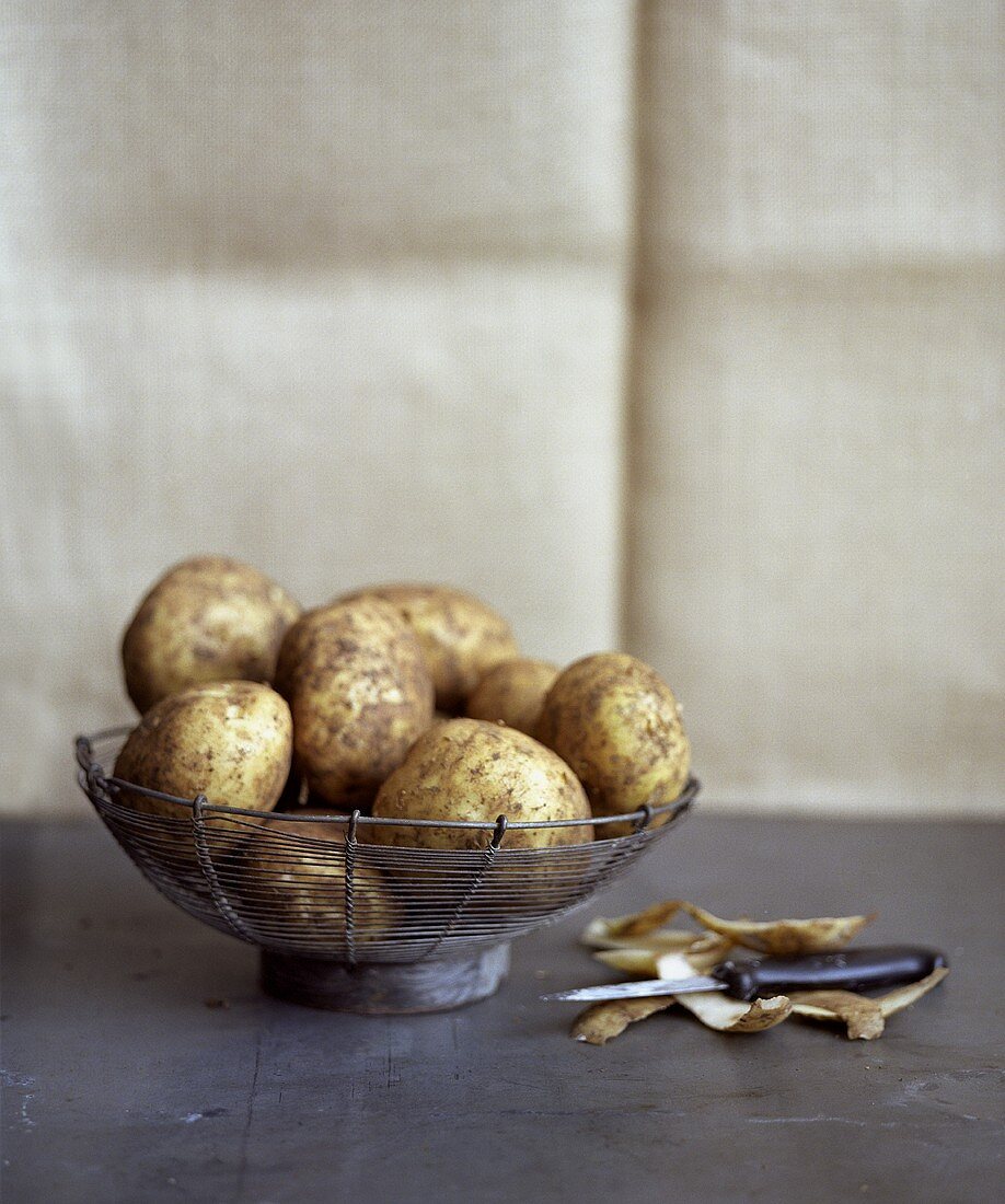 Potatoes in a wire basket, potato peelings beside it