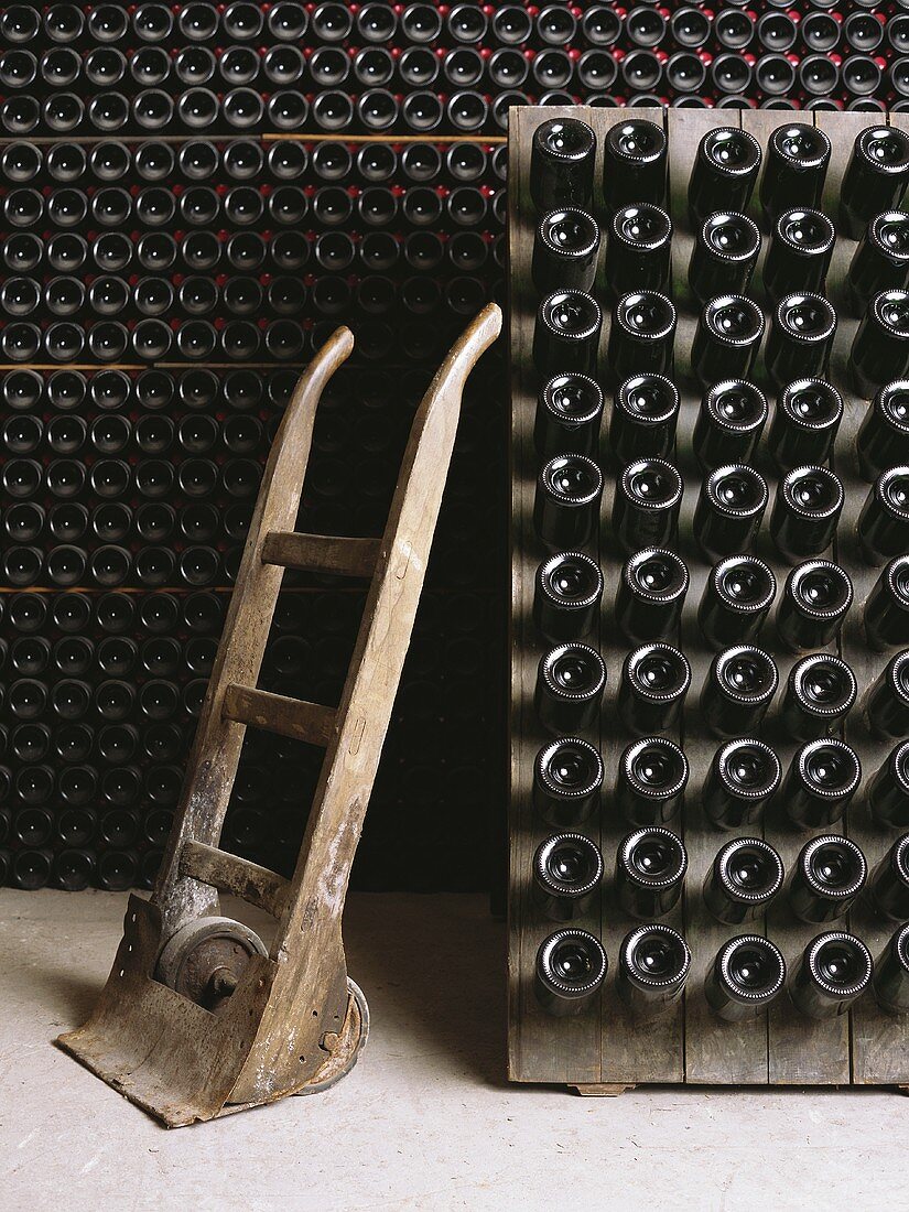 Gestapelte Weinflaschen im Weinkeller und Schubkarre