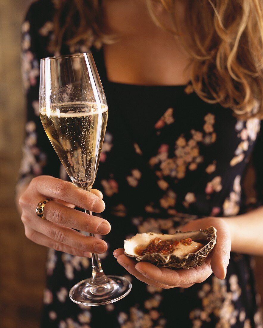 Frau hält Auster mit Chili-Ingwer-Sauce und Glas Champagner