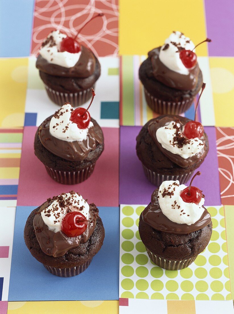 Chocolate muffins with chocolate icing, cream and cherries