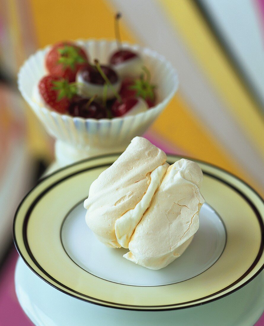 Baiser mit Sahne, im Hintergrund Erdbeeren und Kirschen