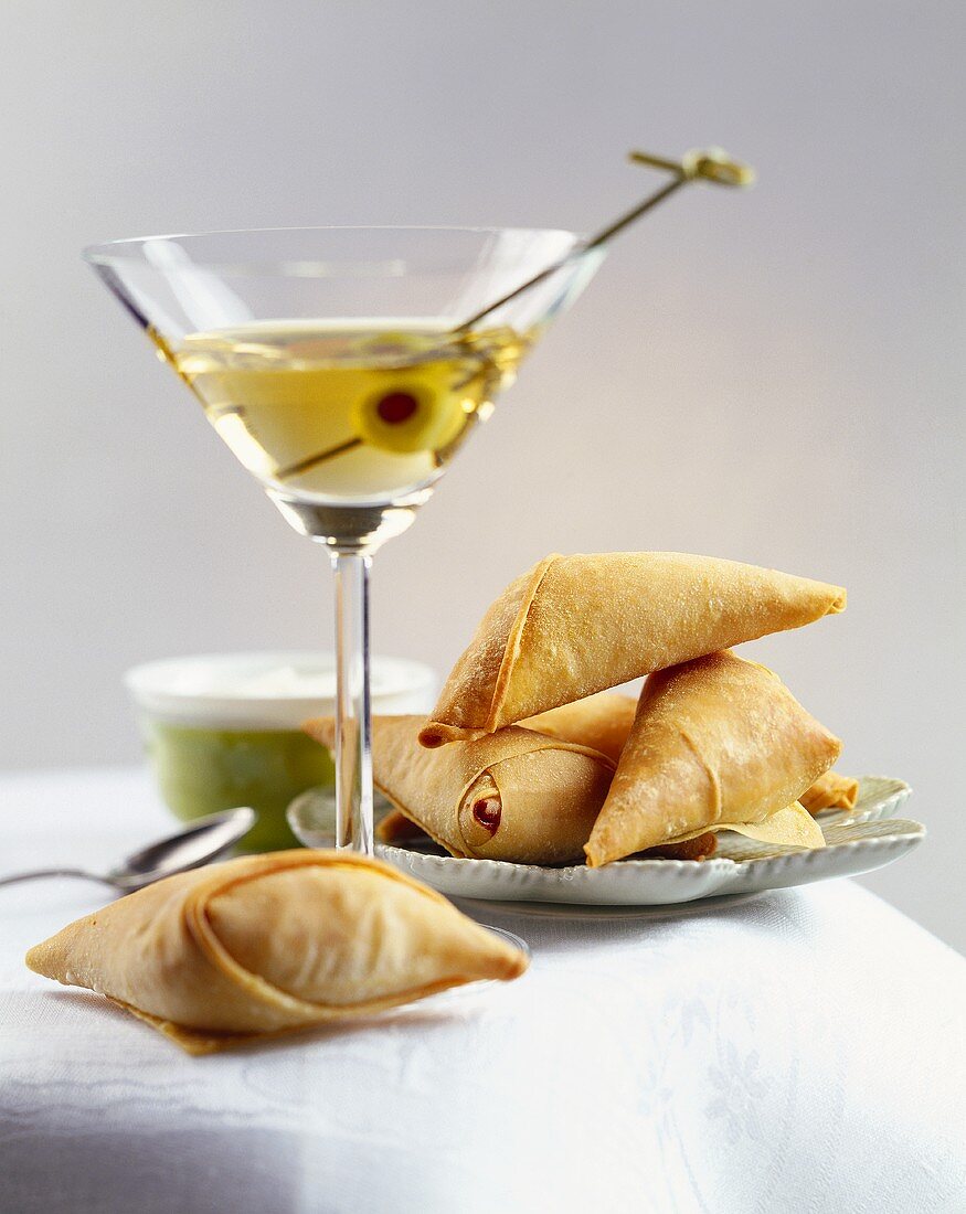 Filled filo pastry triangles & a glass of Martini with olive