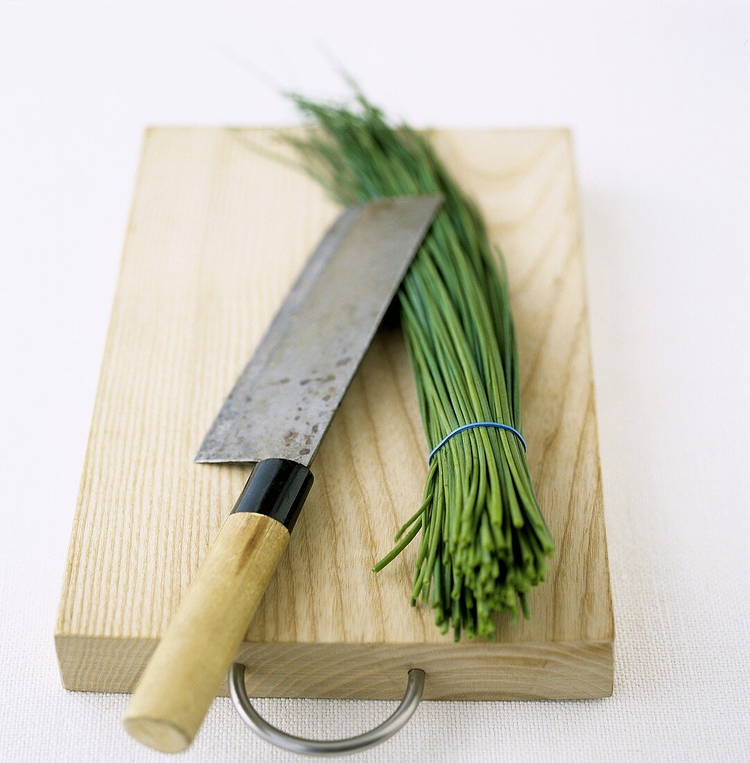 A bunch of chives with knife on wooden board