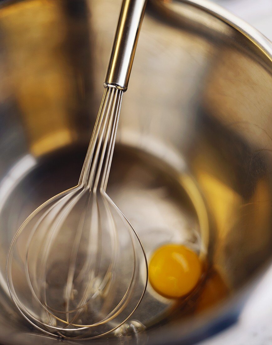 Bowl with egg broken into it and whisk