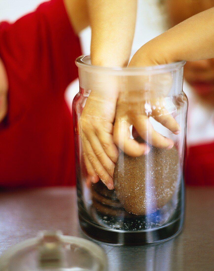 Children's hands reaching for chocolate biscuits in jar 