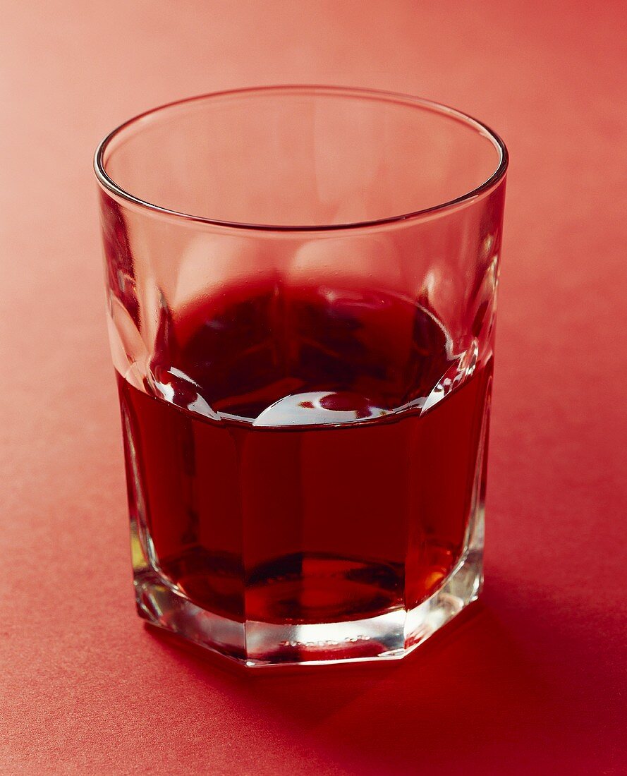 Rotwein im Wasserglas vor rotem Hintergrund