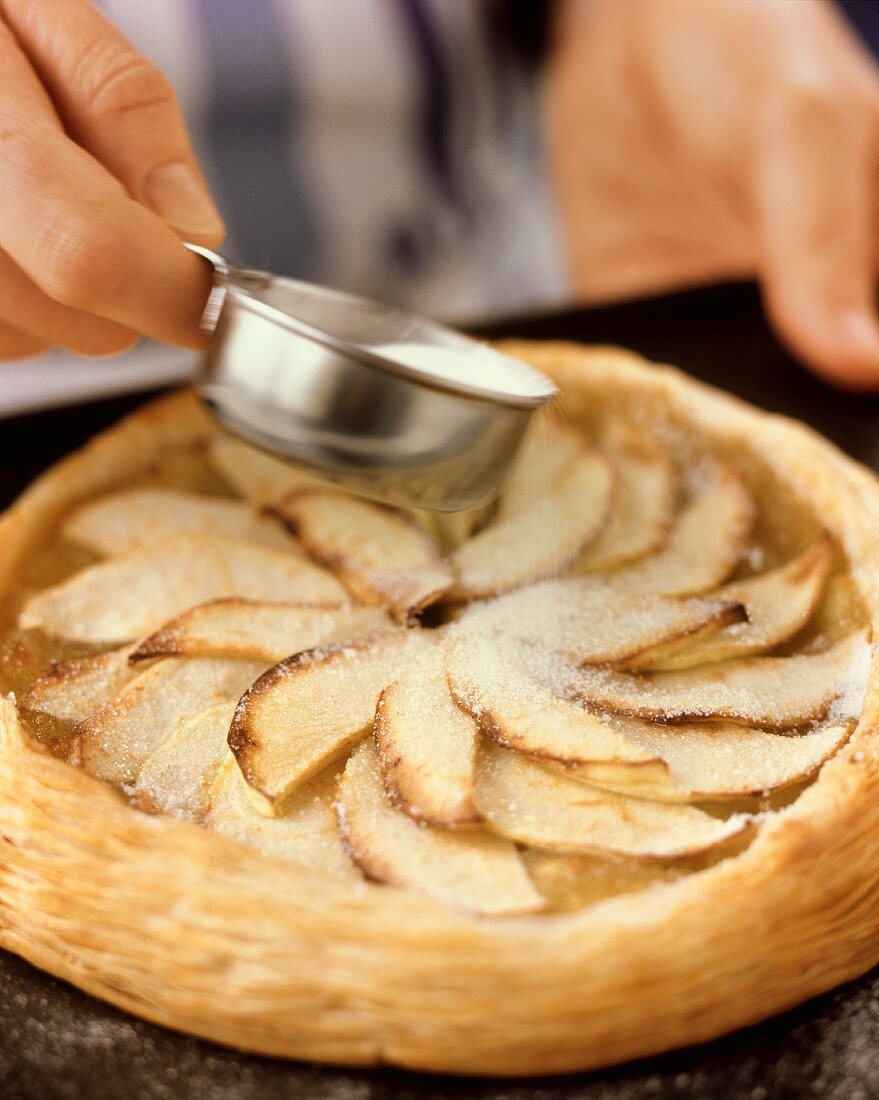 Dusting apple tart with icing sugar