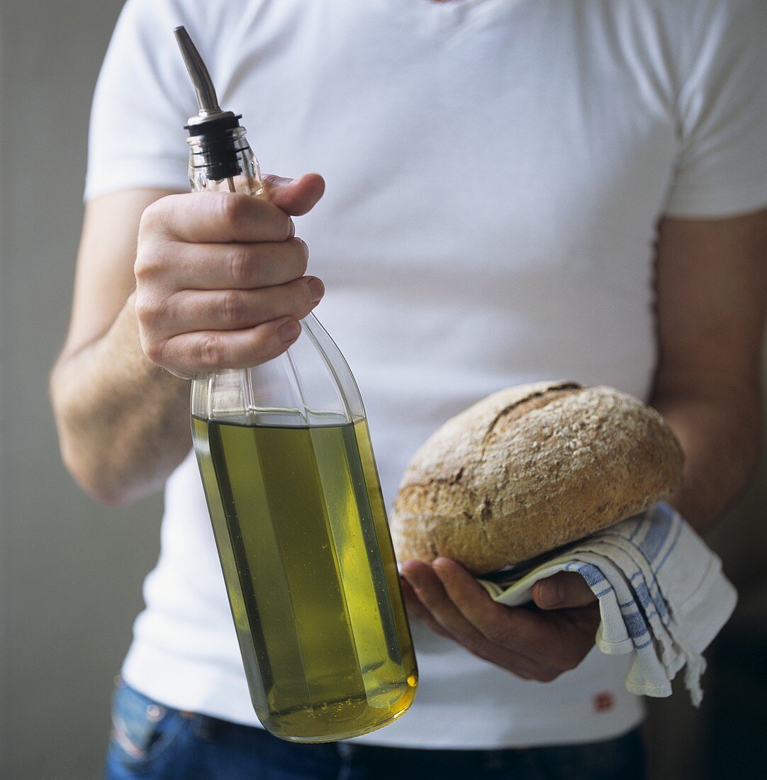 Mann hält eine Flasche Olivenöl und einen Brotlaib