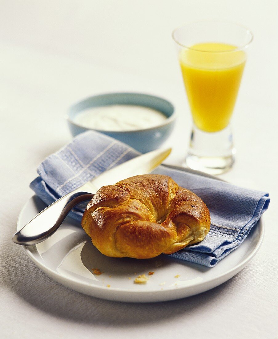 A croissant with a glass of orange juice and yoghurt