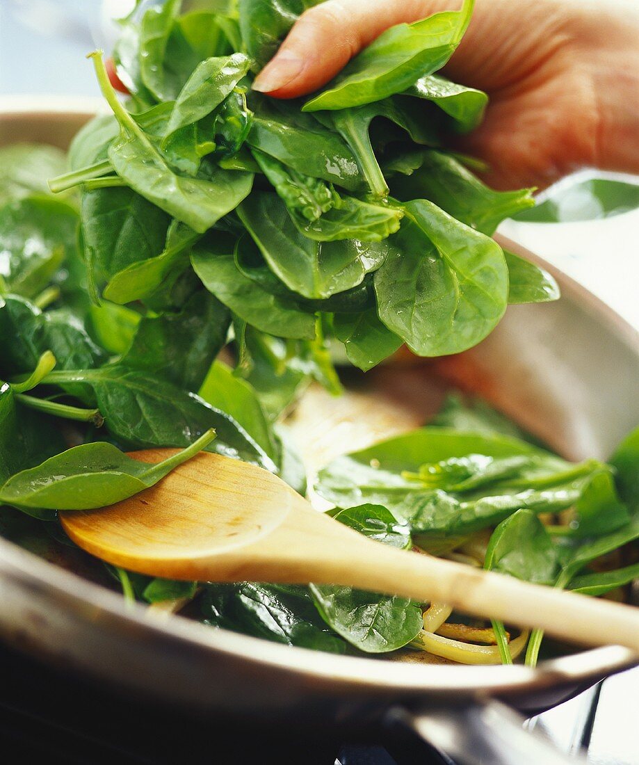 fresh spinach being sautéed in a frying pan