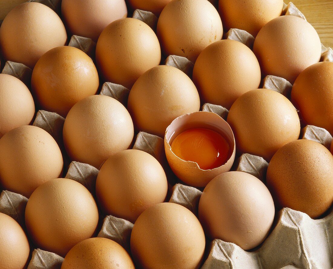 Brown eggs in egg tray, one egg broken open