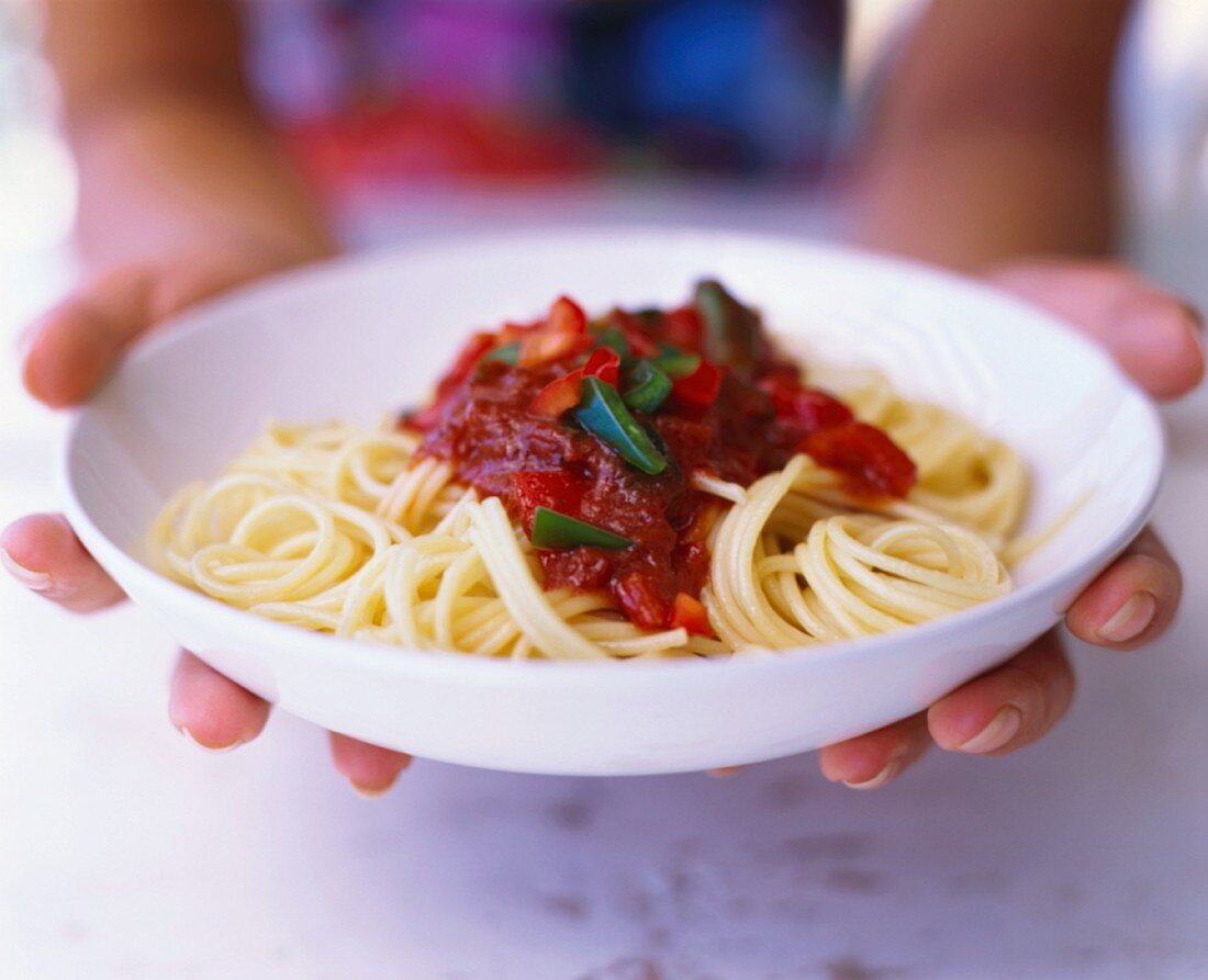 Hands holding a plate of spaghetti and tomato sauce