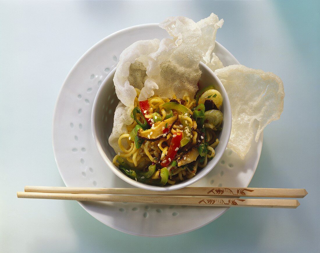 Vegetables, sesame & noodles in small bowl with prawn crackers
