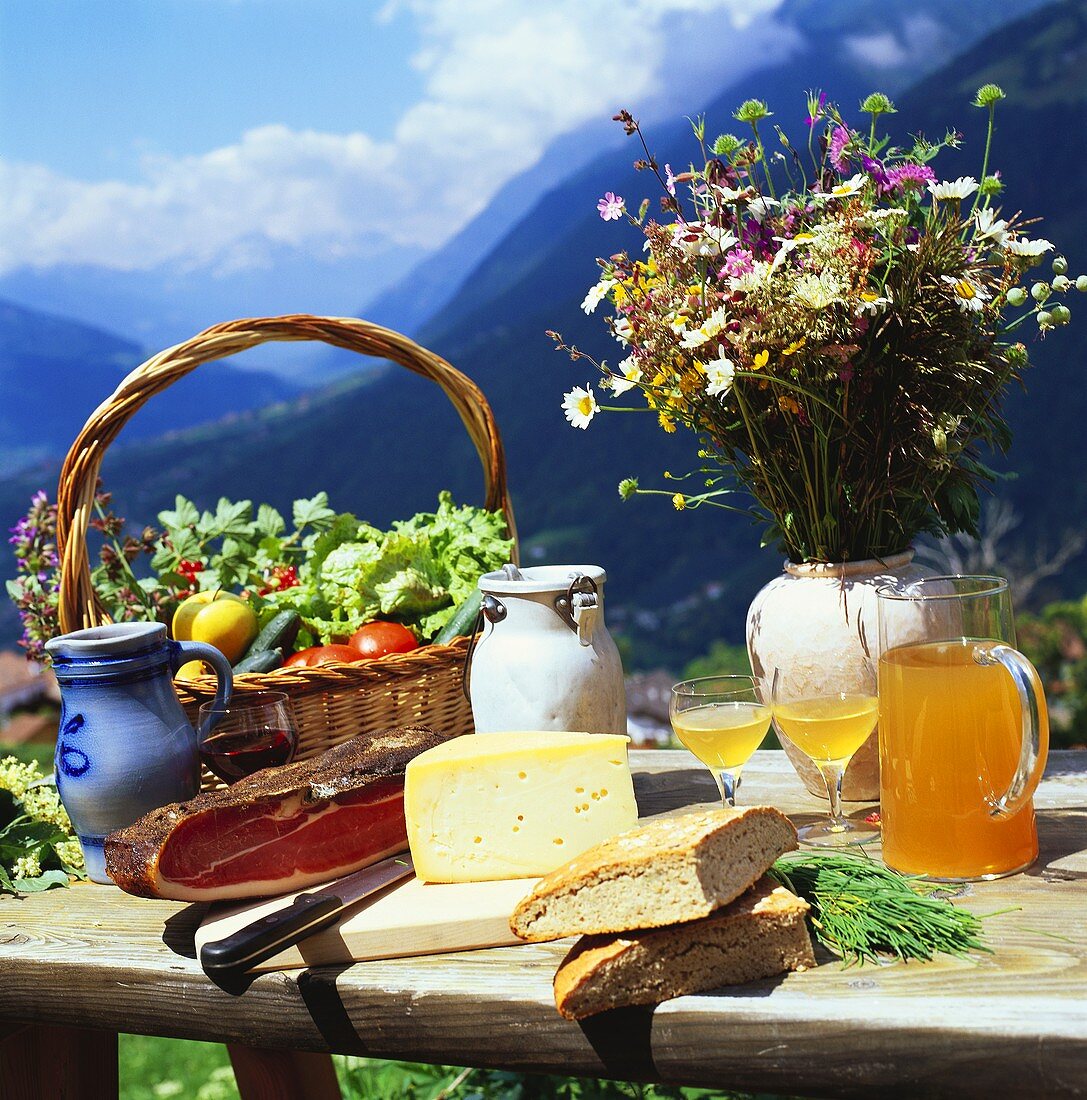Käse, Brot, Gemüse etc. auf Holztisch in Berglandschaft