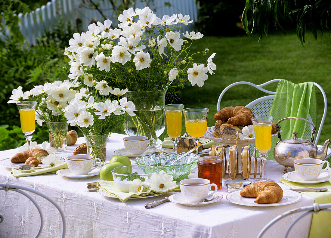 Laid breakfast table with vases of Cosmos, in open air