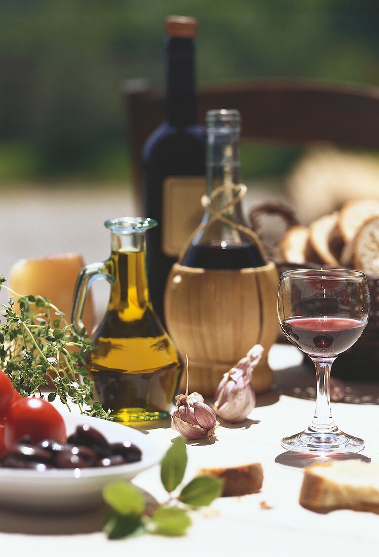 Stillleben mit Oliven, Olivenöl, Rotwein, Knoblauch und Brot
