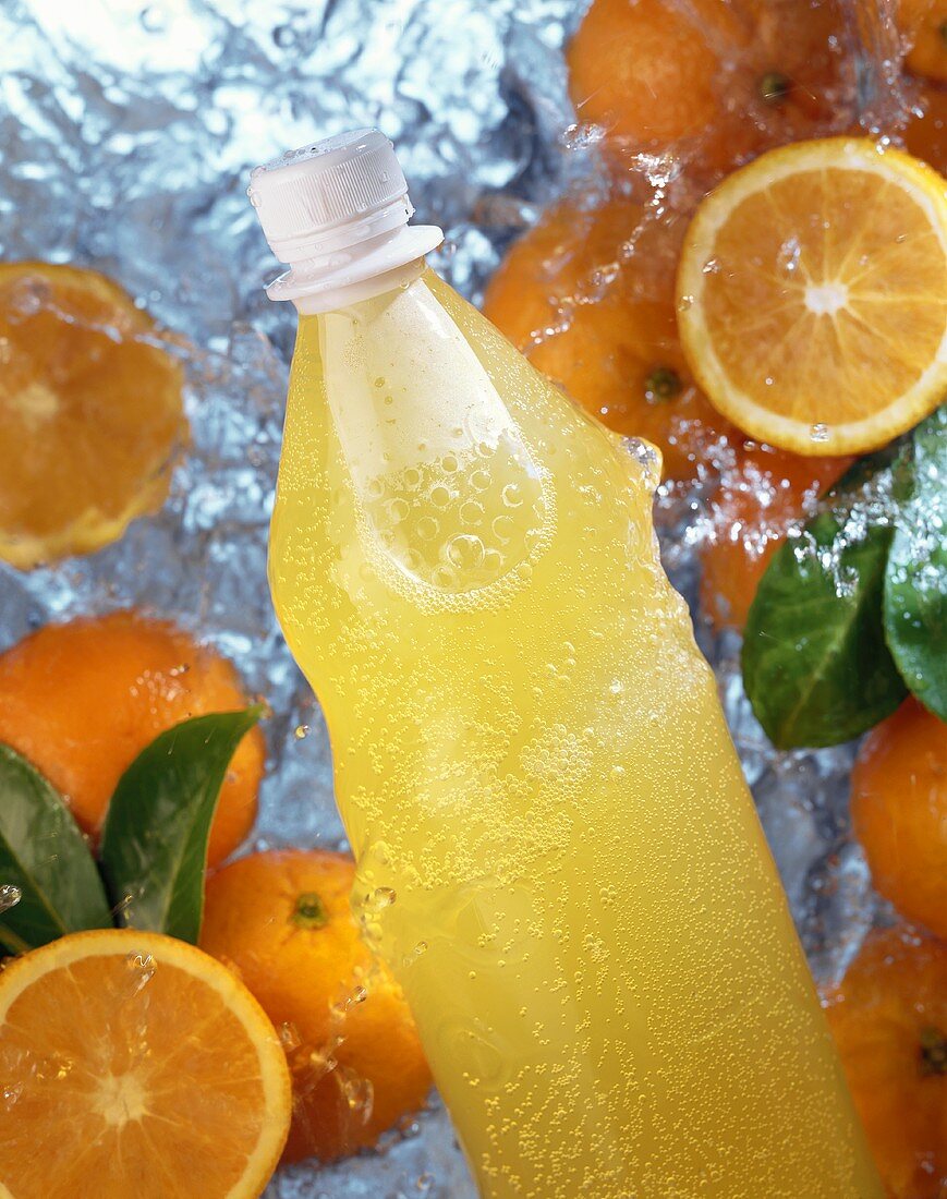 A bottle of orangeade and oranges