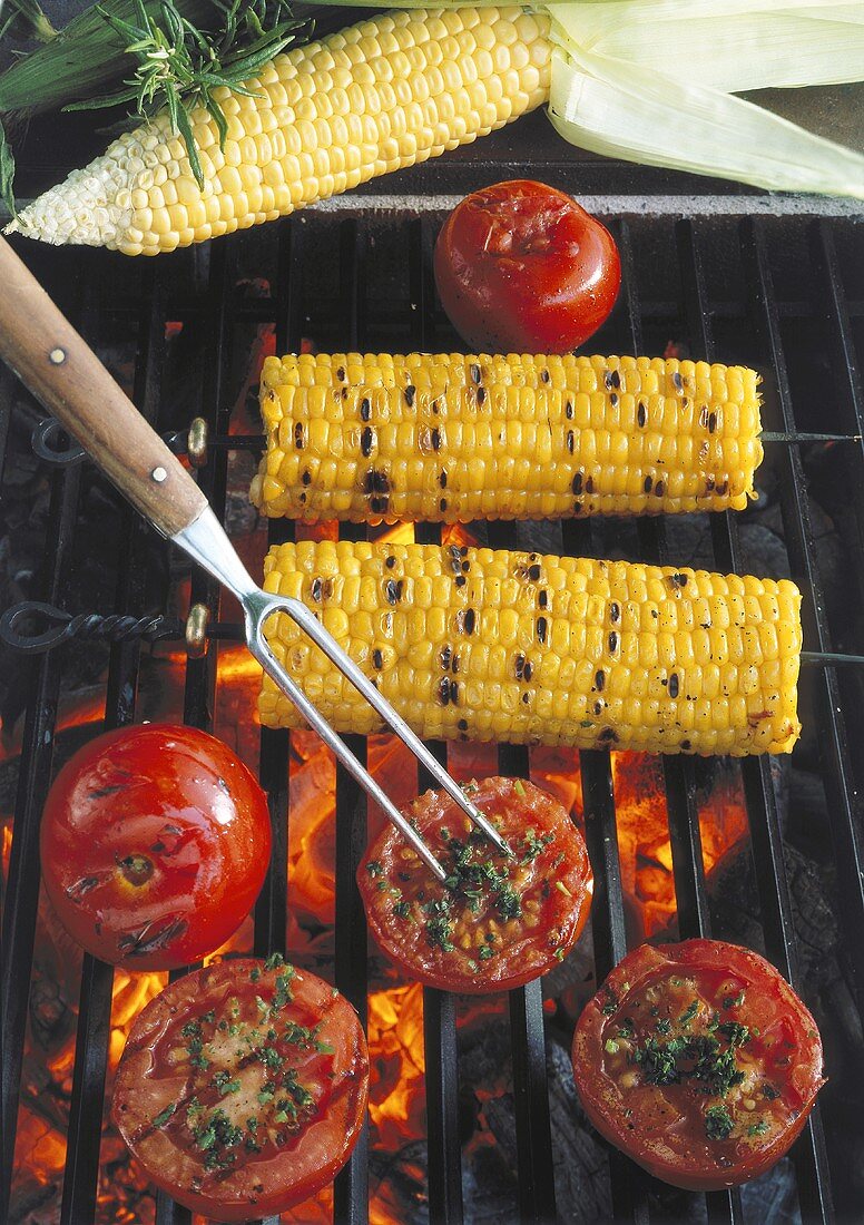 Corncobs and tomatoes with herbs on the barbecue