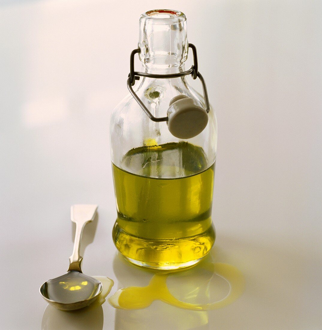 Natives Olivenöl in einer Flasche und auf einem Löffel