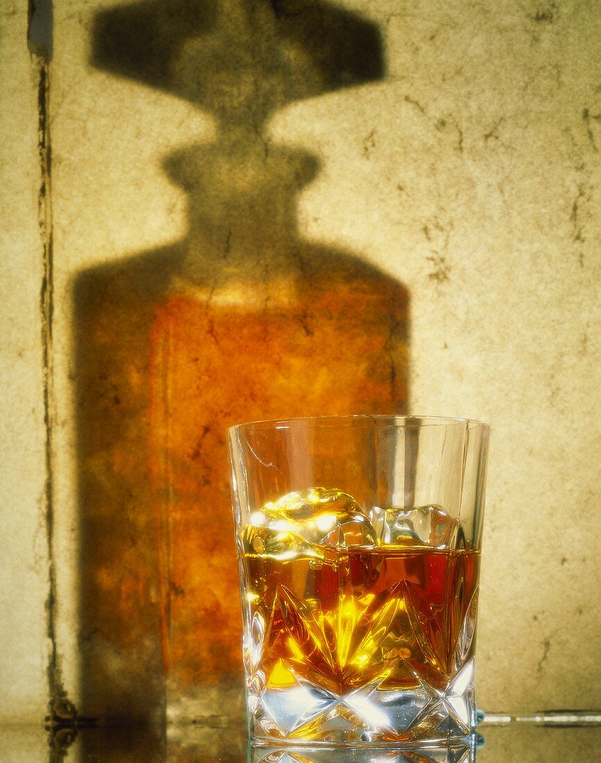 A glass of whisky, shadow of a whisky bottle behind it