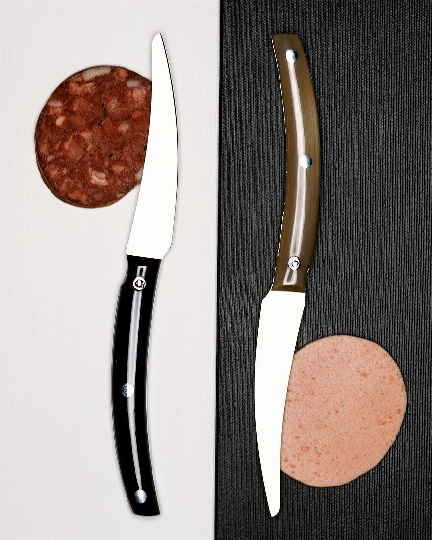 Two knives, each with a slice of sausage